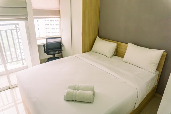 A hotel room with a bed, a chair, and a view of a building through the window. - Studio Room With Cozy Style At Serpong Garden Apartment (Cisauk)