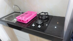 A kitchen with a sink, a pink dish rack, and a gas stove. - Studio Room With Cozy Style At Serpong Garden Apartment (Cisauk)