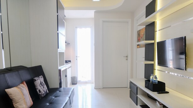 A modern living room with a black leather sofa, a flat-screen TV mounted on the wall, and a white entertainment unit. - Homey And Cozy 2Br Apartment At Parahyangan Residence (Bandung)