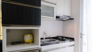 A compact kitchen with white cabinets, a black countertop, a gas stove, and a yellow appliance. - Homey And Cozy 2Br Apartment At Parahyangan Residence (Bandung)