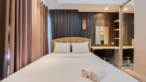 A hotel room with a large bed, a desk, a chair, and a mirror.