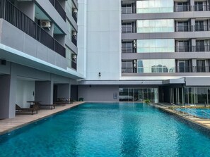 A modern building with a central swimming pool, balconies, and a covered seating area. - Comfort 1Br At Ciputra World 2 Apartment (Jakarta)