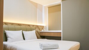 A neatly made bed with white linens and a rolled towel, a wooden headboard, and a bedside table with a lamp.