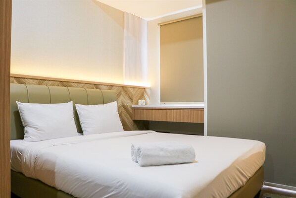 Una cama bien hecha con sábanas blancas y una toalla enrollada, un cabecero de madera y una mesita de noche con una lámpara.