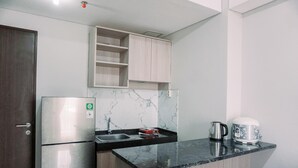 A compact kitchen with a refrigerator, a sink, a marble backsplash, and a kettle on the countertop. - Comfortable And Homey 2Br At Transpark Bintaro Apartment (South Tangerang)