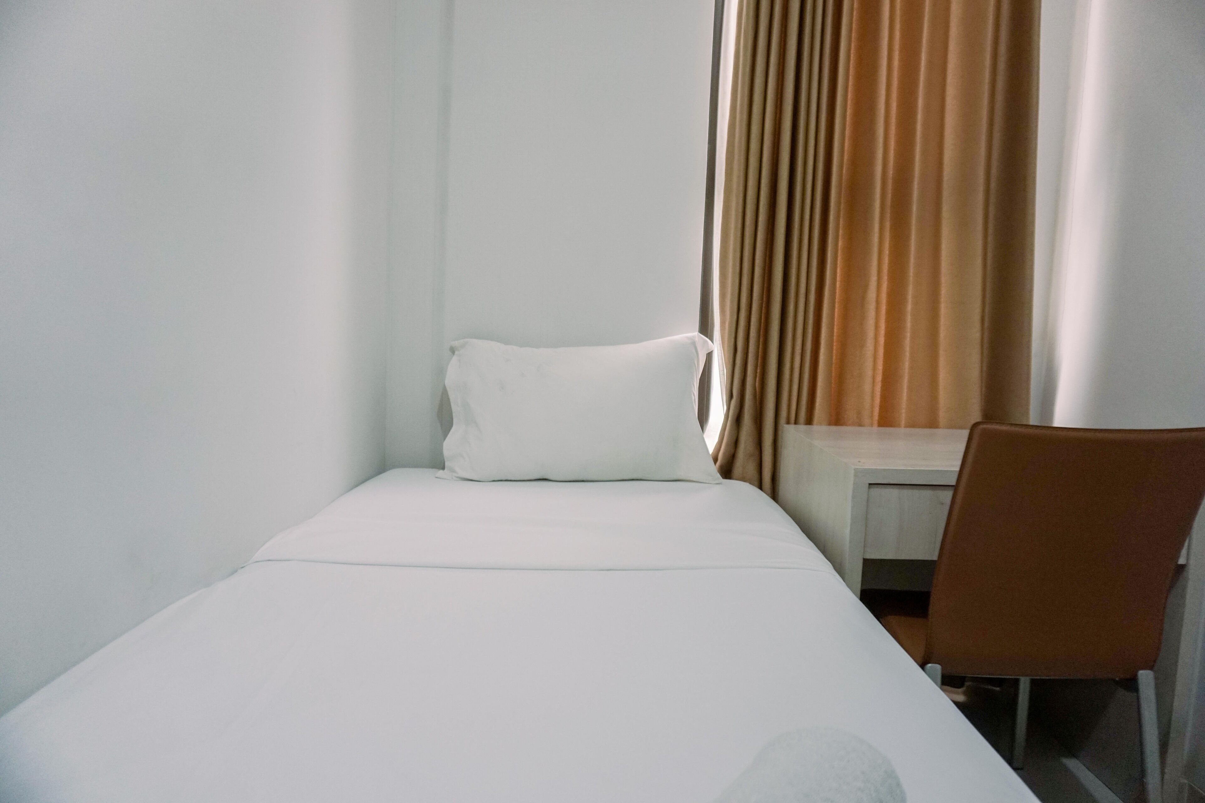 A small, single-bed room with a white bed, a chair, and a desk.