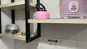 A kitchen with a pink kettle, a rice cooker, and a frying pan on a shelf.