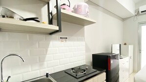 A kitchen with a sink, stove, and a refrigerator. There are shelves above the stove holding kitchenware.