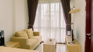 Une chambre d’hôtel moderne avec un canapé beige, une table d’appoint en bois, une télévision et une petite plante posée sur une étagère.