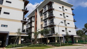 Un immeuble résidentiel à plusieurs étages, doté de balcons, d’une entrée couverte et d’un jardin aménagé.