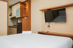 A hotel room with a bed, a TV mounted on the wall, a small table, and a kitchenette area.