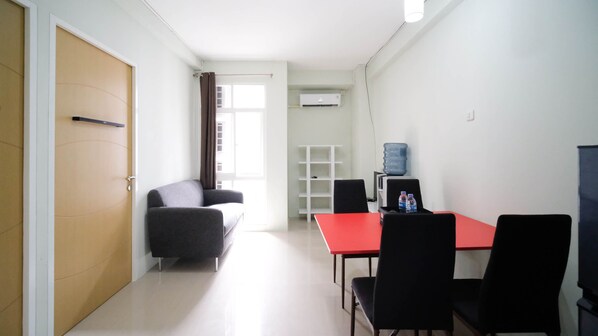 A small, well-lit room with a red table and black chairs, a grey sofa, a white shelf, and a water dispenser. - Best Deal And Homey 2Br At Bale Hinggil Apartment (Surabaya)