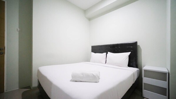 Una cama bien hecha con sábanas y almohadas blancas, un cabecero tapizado de color negro y una mesita de noche blanca con un cajón.
