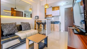 A modern living room with a sofa, a coffee table, and a kitchen area in the background. - Cozy 2Br Transpark Cibubur Apartment Near Mall (Depok)