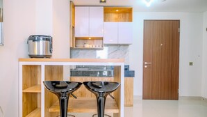 A compact kitchen with a microwave, wooden cabinets, and a countertop with a sink. There are two black bar stools in front of the counter. - Cozy 2Br Transpark Cibubur Apartment Near Mall (Depok)