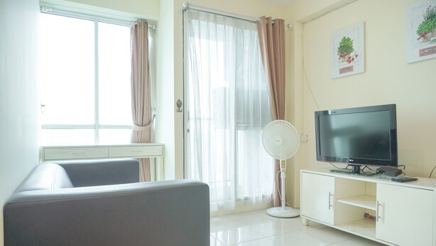 A living room with a sofa, a TV on a white cabinet, a fan, and a sliding glass door with curtains.