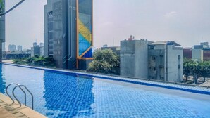 A swimming pool with a tiled deck and metal railings, surrounded by buildings with modern architecture.