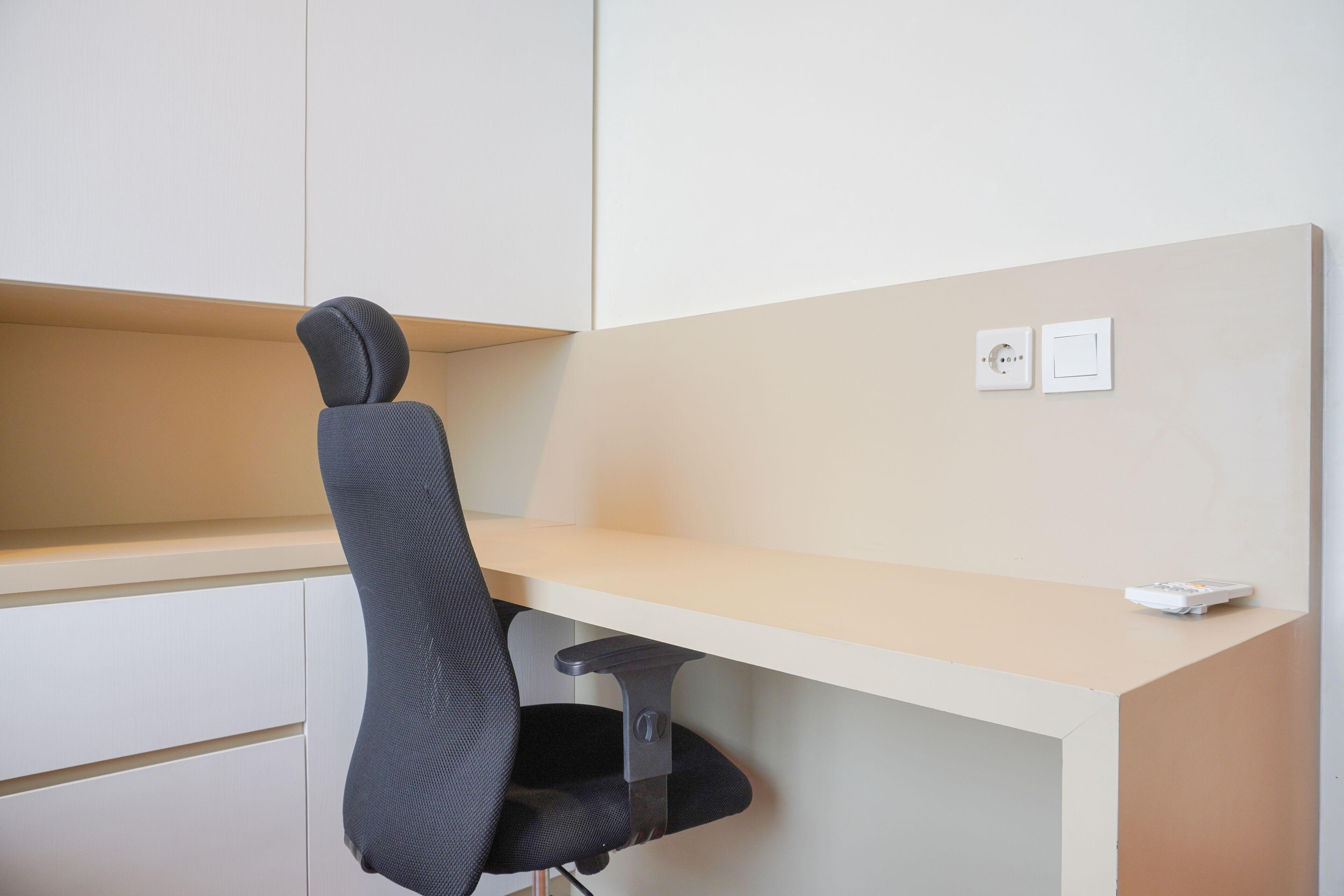 A modern office cubicle with a black office chair, a beige desk, and two white switches on the wall.