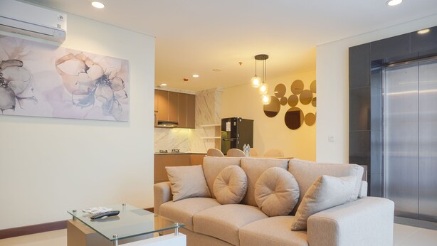 A modern living room with a beige sofa, a glass coffee table, and a kitchen in the background.