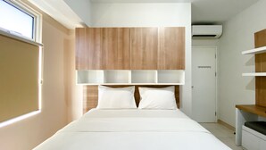 Un dormitorio moderno con una cama grande, cabecero de madera integrado, ropa de cama blanca y una ventana que proporciona luz natural.