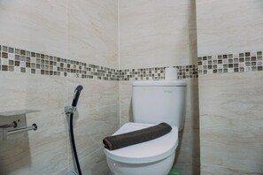 Une salle de bain équipée de toilettes, d’un flexible de douche et d’un mur carrelé.