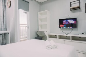 Une chambre d’hôtel moderne, équipée d’un lit, d’un téléviseur fixé au mur et d’un balcon visible à travers une porte ouverte.