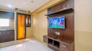 Una sala moderna con televisor de pantalla plana montado en un mueble de madera, una zona de cocina con armarios y una puerta corrediza de vidrio con cortinas anaranjadas.
