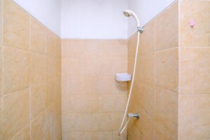 Une douche aux carreaux beiges, un pommeau de douche blanc et un porte-savon.