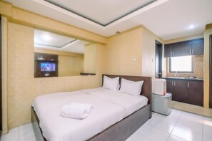 Une chambre d’hôtel avec un grand lit, une petite table de chevet, un téléviseur fixé au mur et un coin cuisine.