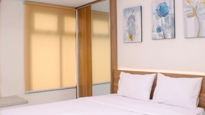 Een hotelkamer met een bed, een nachtkastje, een raam met jaloezieën en drie schilderijen aan de muur.