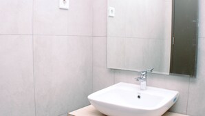 Een moderne badkamer met een witte wastafel, een spiegel en lichtgekleurde tegels.