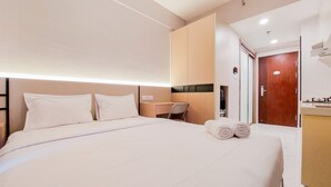 A hotel room with a large bed, a desk, and a wooden wardrobe. - Best Deal And Simply Look Studio Room At Sky House Bsd Apartment (Pagedangan)