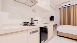 A modern hotel room with a kitchenette, a bed, a flat-screen TV, and a window with curtains. - Best Deal And Simply Look Studio Room At Sky House Bsd Apartment (Pagedangan)