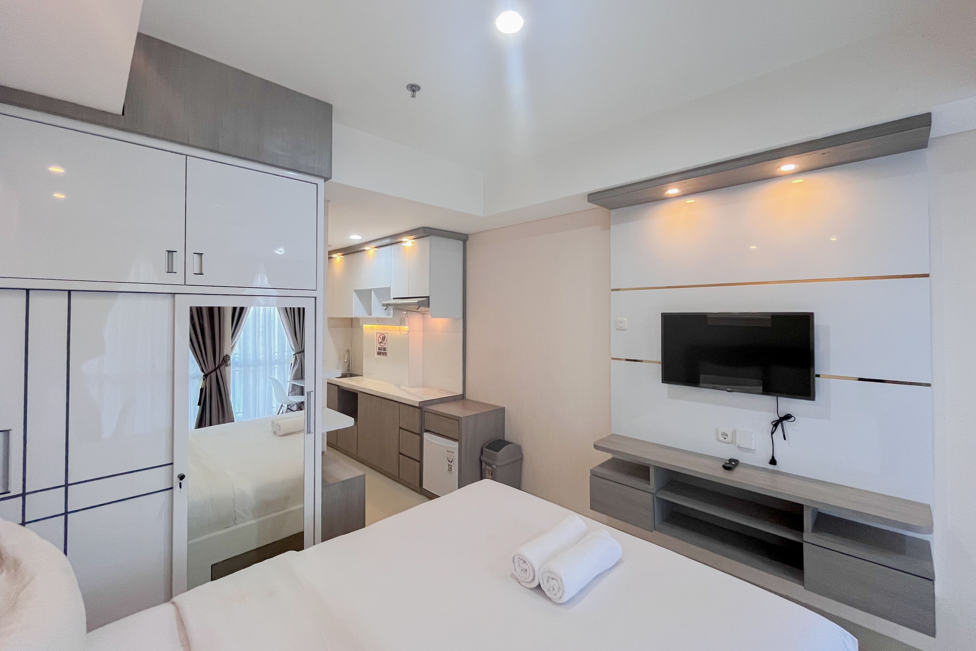 A modern hotel room with a bed, a TV, a desk, and a wardrobe.