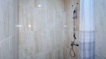 A bathroom with marble tiles, a shower with a handheld showerhead, and a striped shower curtain.