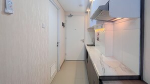 Un couloir étroit avec une porte blanche, un interphone fixé au mur, et un coin cuisine doté d’un plan de travail en marbre et d’une cuisinière.