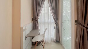 Une petite pièce moderne comprenant un coin cuisine, un espace repas avec une chaise blanche et une grande fenêtre ornée de rideaux légers.