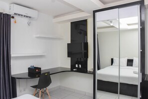 A hotel room with a bed, a desk, a chair, a TV, and a wardrobe. - Comfy And Tidy Studio Amethyst Apartment (Jakarta)