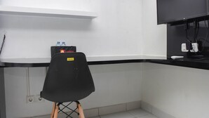 Una pequeña cocina americana con una silla negra, un estante con botellas de agua y un televisor de pantalla plana montado en la pared.