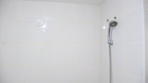 Un baño con paredes de azulejos blancos, una ducha con cabezal de ducha manual y un enchufe en la pared.