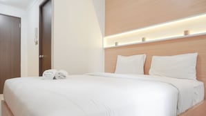A neatly made bed with white linens, a wooden headboard, and a bedside table with a lamp.