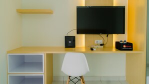 A modern workspace with a flat-screen TV, a small black speaker, and a travel bag on a desk. - Comfortable And Minimalist Studio At Amethyst Apartment (Jakarta)