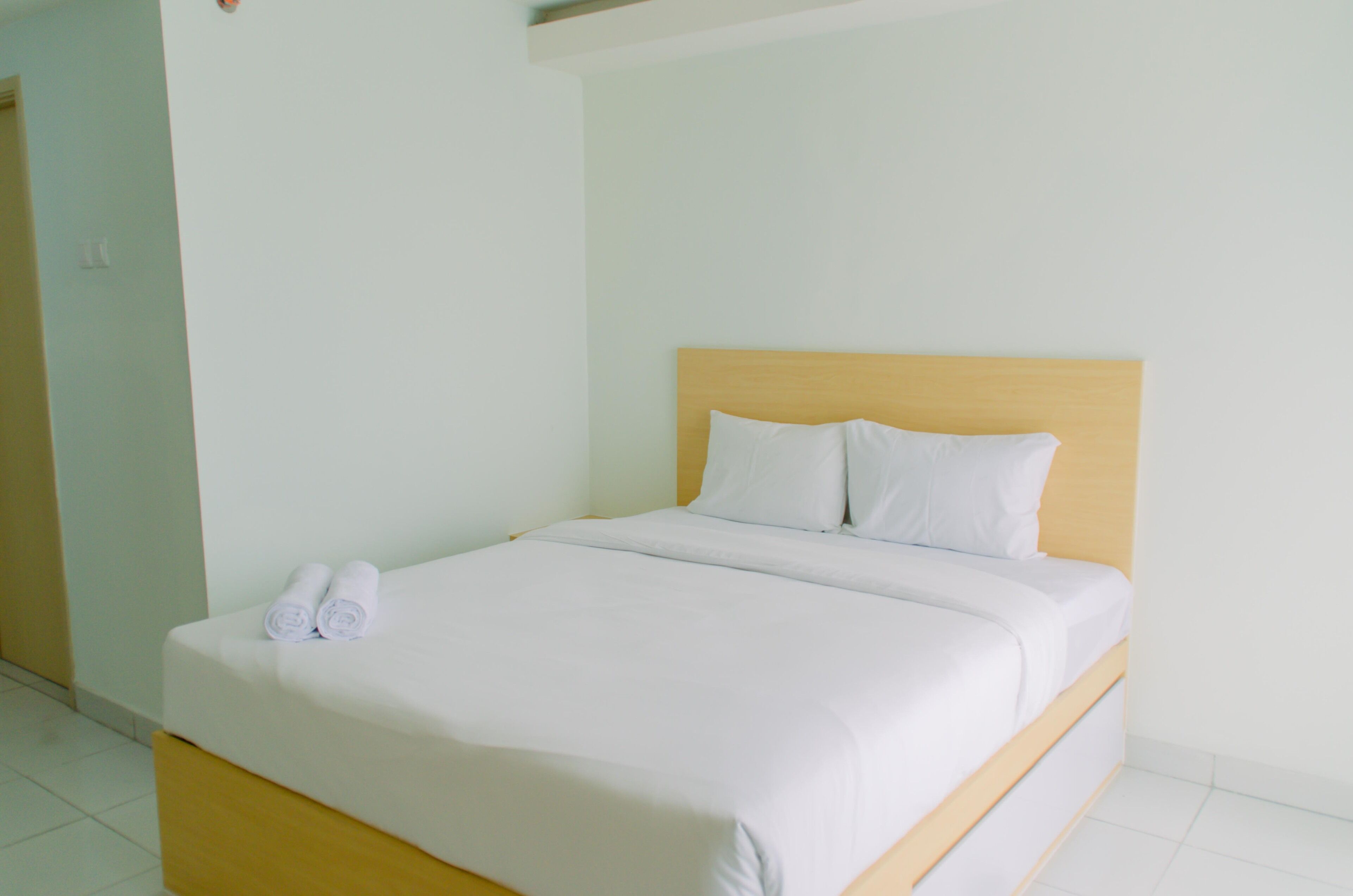 A neatly made bed with white linens and two rolled towels on the footboard.