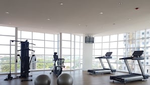 A spacious gym with large windows, a variety of exercise equipment, and a wooden floor. - Minimalist And Nice Studio At Tree Park City Cikokol Apartment (Tangerang)
