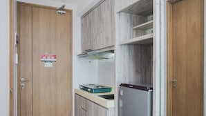 A compact kitchen with wooden cabinets, a gas stove, and a refrigerator. - Minimalist And Nice Studio At Tree Park City Cikokol Apartment (Tangerang)
