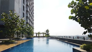 A swimming pool with a tiled edge, surrounded by greenery and a modern building. - Minimalist And Nice Studio At Tree Park City Cikokol Apartment (Tangerang)