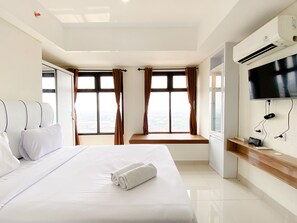 A hotel room with a large bed, two windows with curtains, a flat-screen TV mounted on the wall, and a wooden bench by the windows. - Modern Look Studio At Pollux Chadstone Apartment (Cikarang)