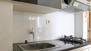 Cozinha com pia de aço inoxidável, fogão a gás e paredes com azulejos brancos.
