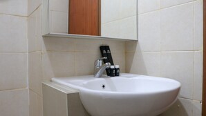 Uma pia branca com uma única torneira, um espelho acima e um armário de madeira à direita.