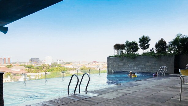 Une piscine extérieure à débordement offrant une vue sur le paysage urbain, entourée d’une terrasse en bois et de murs en pierre.
